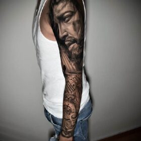 tatuaje realista de rostro de cristo en todo el brazo con rosas y brujula sombras
