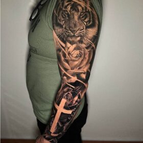 tigre tatuado en brazo con rosas y cruz en blanco y negro
